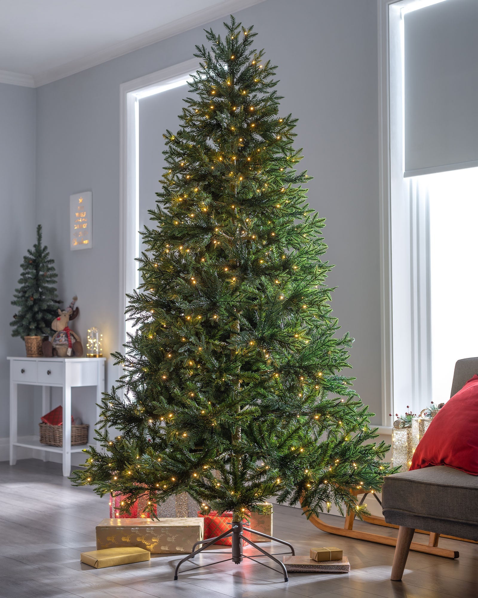 Pre-lit Mountain Pine Christmas tree with natural bark and warm white LED lights, standing indoors with realistic green branches and festive decorations.