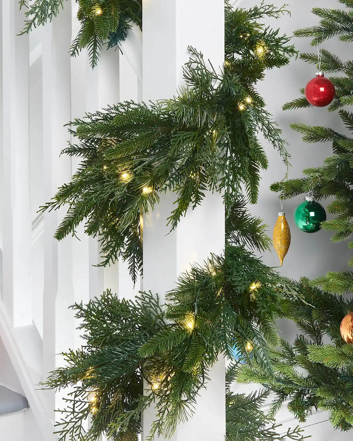 Pre-Lit Natural Fir Garland, 18 ft on a staircase wooden white banister, multi coloured baubles on a Christmas Tree