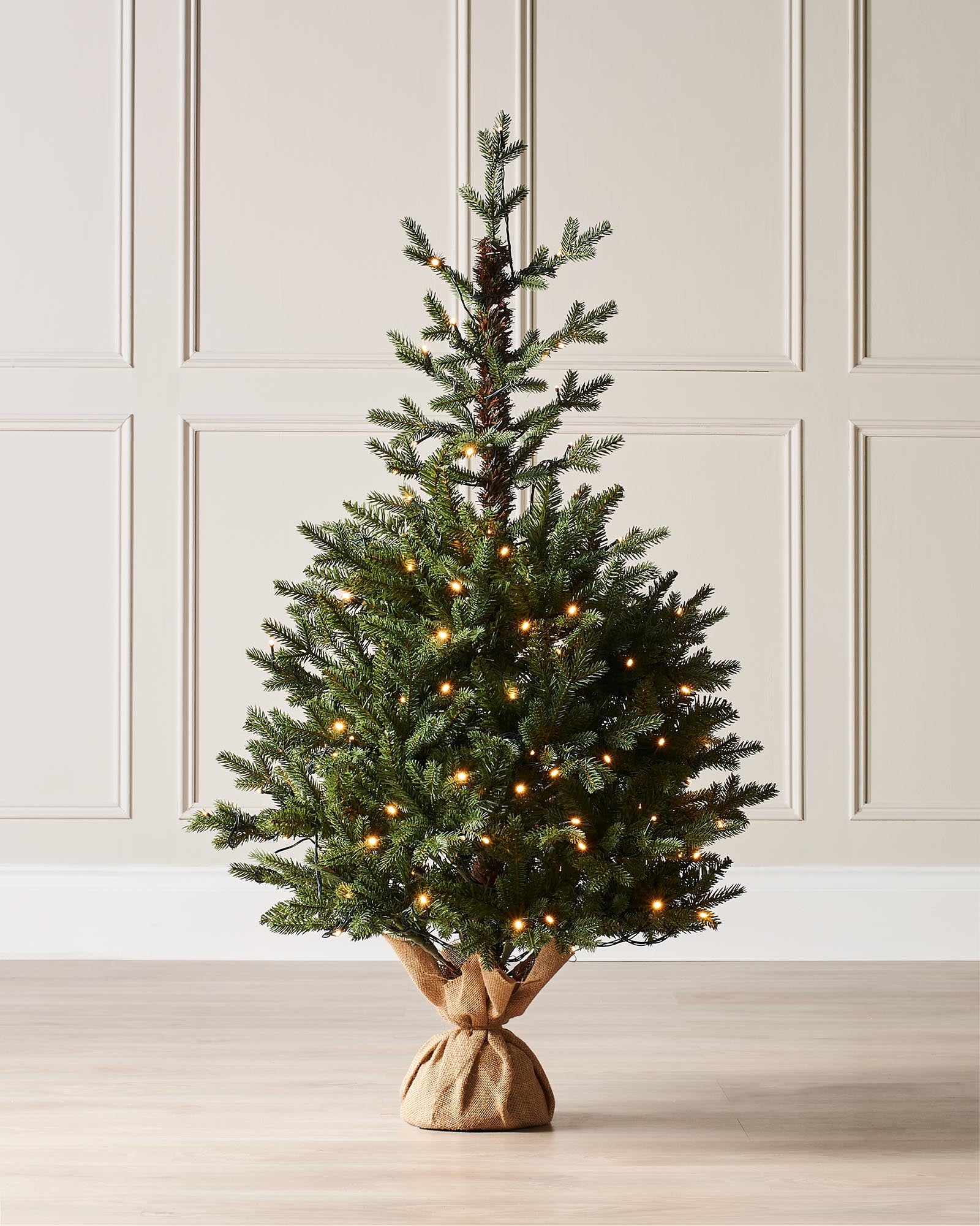 Pre-lit Norway Spruce potted Christmas tree with realistic green branches, warm white LED lights, and a rustic hessian-wrapped base.