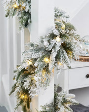 Pre-Lit Snow-Flocked Fir Garland, 18 ft on White wooden staircase banister with a snow globe on a table 