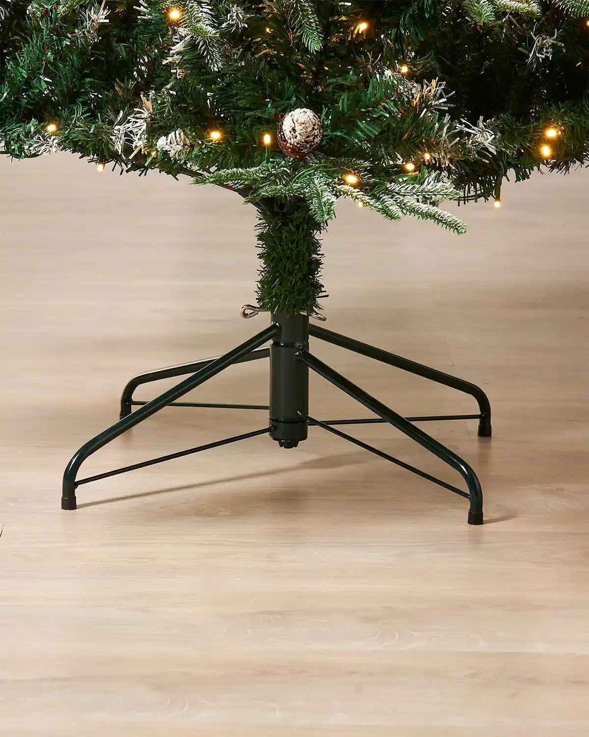 Close up of Black tree stand and base of tree on Pre-Lit Snow Flocked Norwegian Spruce Christmas Tree with Pine cones and Red berries, 7ft
