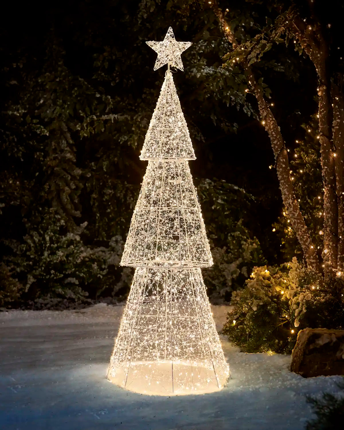 Pre-Lit Twinkling Beaded Christmas Tree glowing with warm white lights in a snowy outdoor garden at night