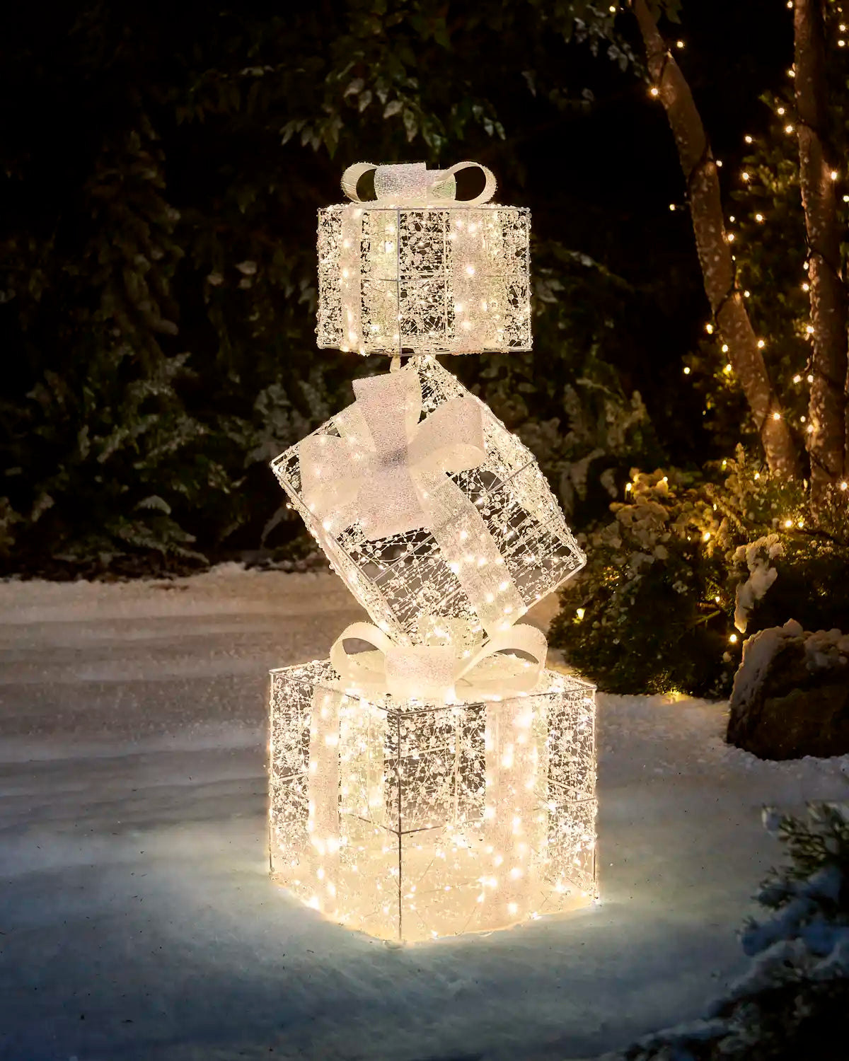 Pre-Lit Twinkling Present Stack glowing with warm white lights in a snowy outdoor garden at night