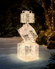 Pre-Lit Twinkling Present Stack glowing with warm white lights in a snowy outdoor garden at night