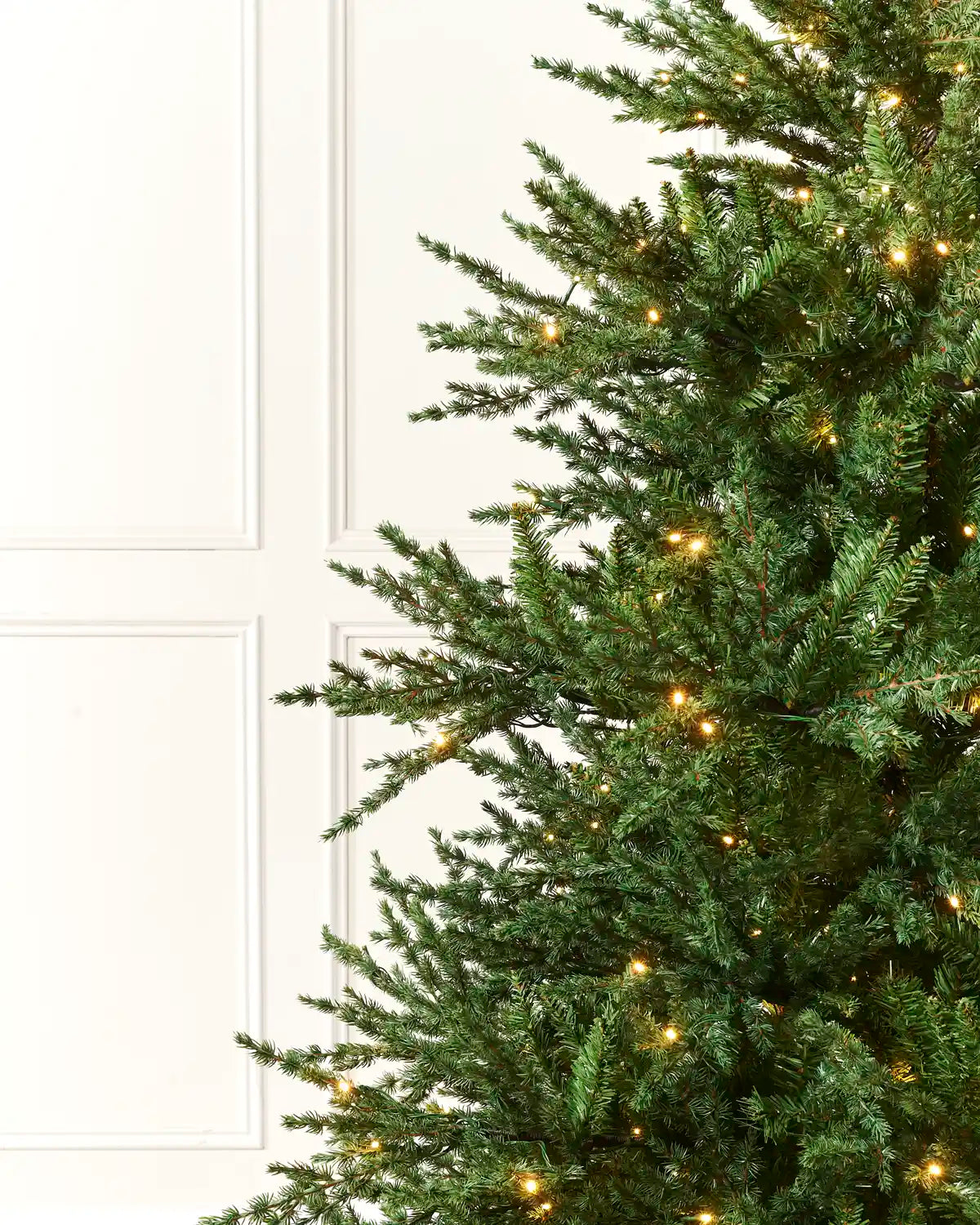 Close-up of realistic green branches and warm white lights on the traditional fir Christmas tree
