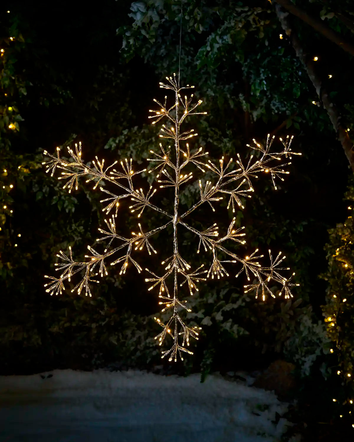 Pre Lit hanging warm white snowflake star against a winter garden setting