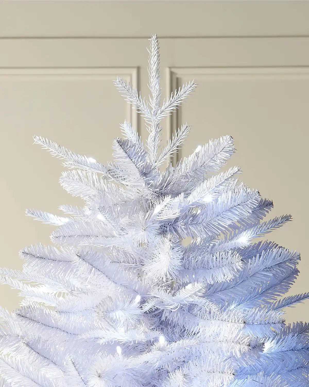 Top portion of 6ft pre-lit white pine Christmas tree in front of white panelling 
