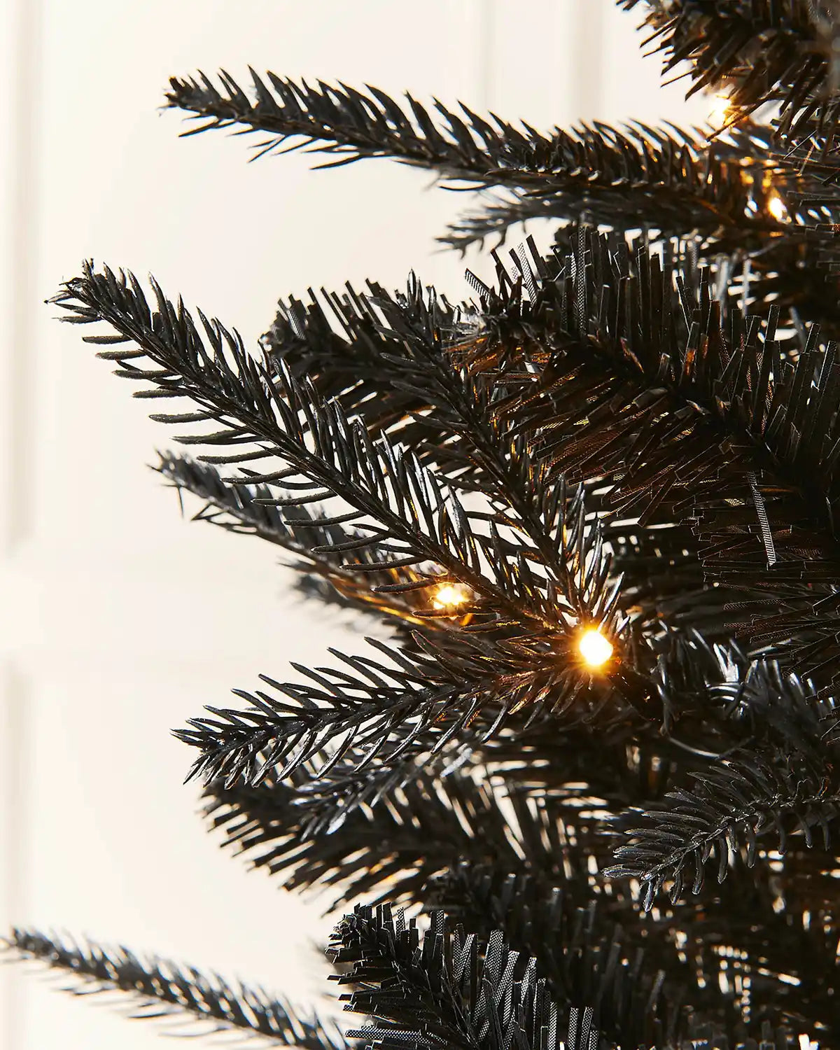 Close-up of 7ft pre-lit black pine Christmas tree branches with warm light setting and white panelling background