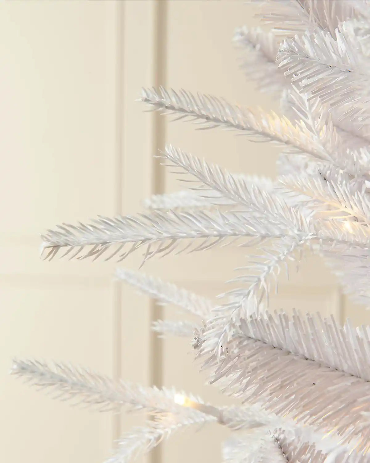 Close-up pre-lit 7ft white pine Christmas tree with bright white lighting in front of white panelling