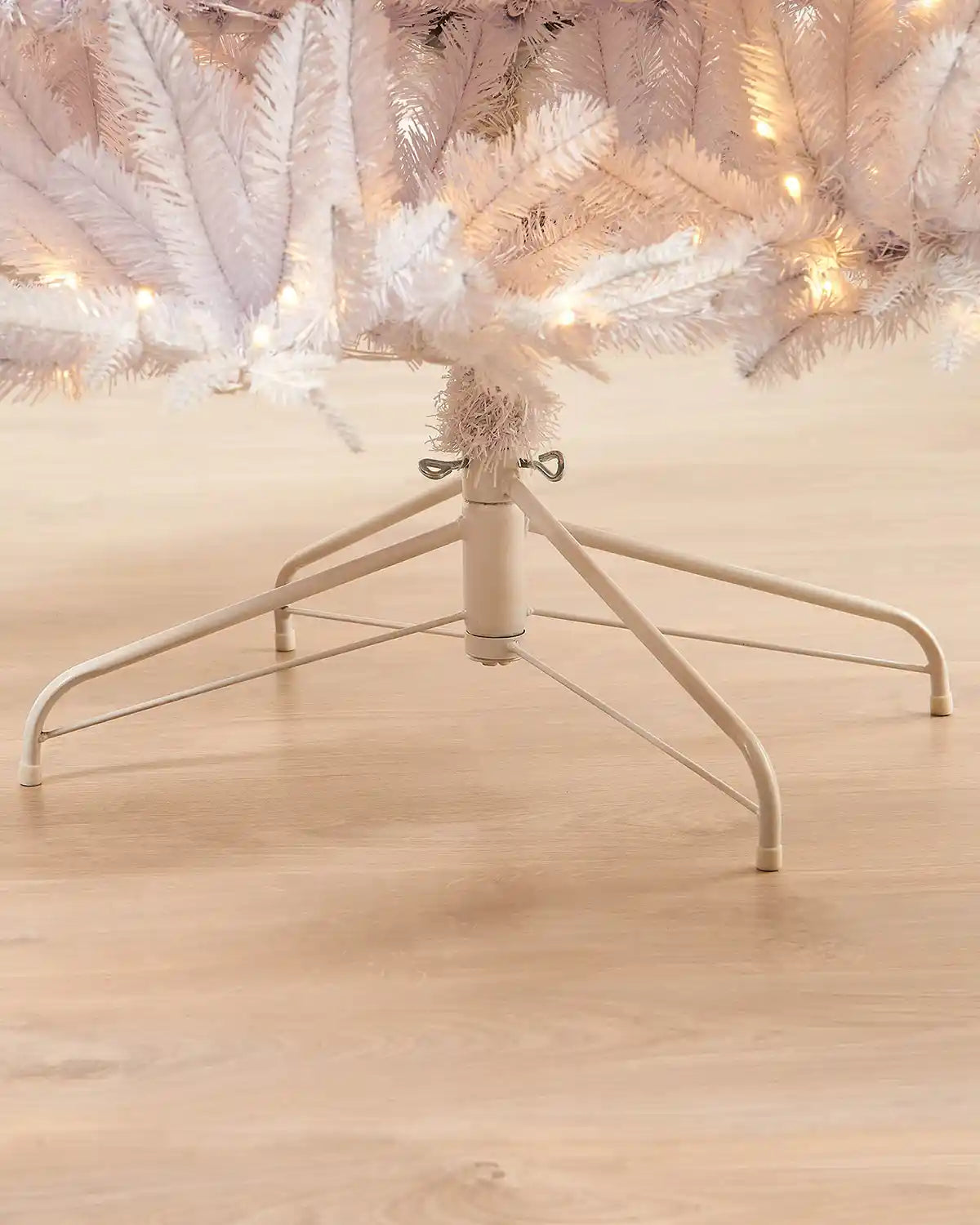 Close-up of cream white stand holding 7ft pre-lit white pine Christmas tree on light wooden floor