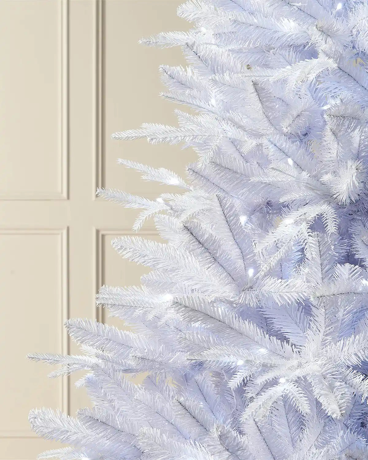 Close-up of 8ft pre-lit white pine tree branches with bright white lighting in front of white panelling 