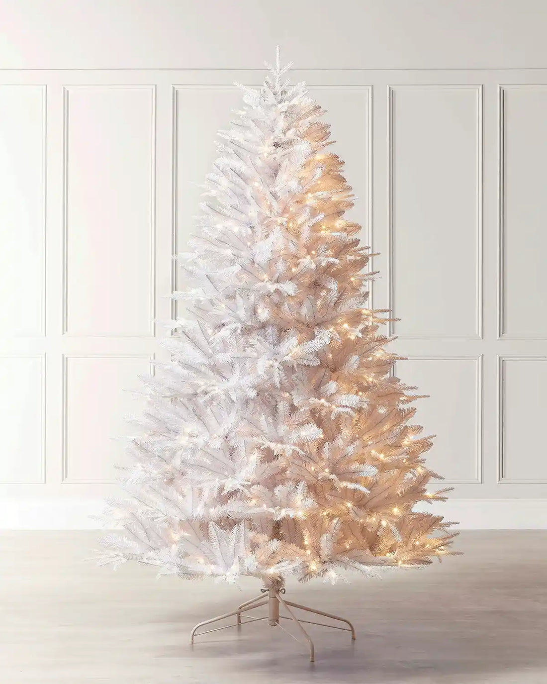 Full image of 7ft pre-lit white pine Christmas tree including stand on light wood flooring in front of white panelling