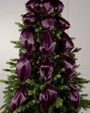 Purple satin ribbon draped and arranged on a green Christmas tree.