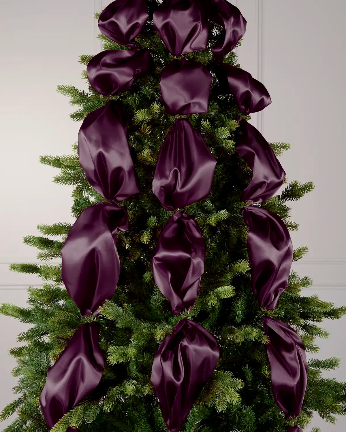 Purple satin ribbon draped and arranged on a green Christmas tree.