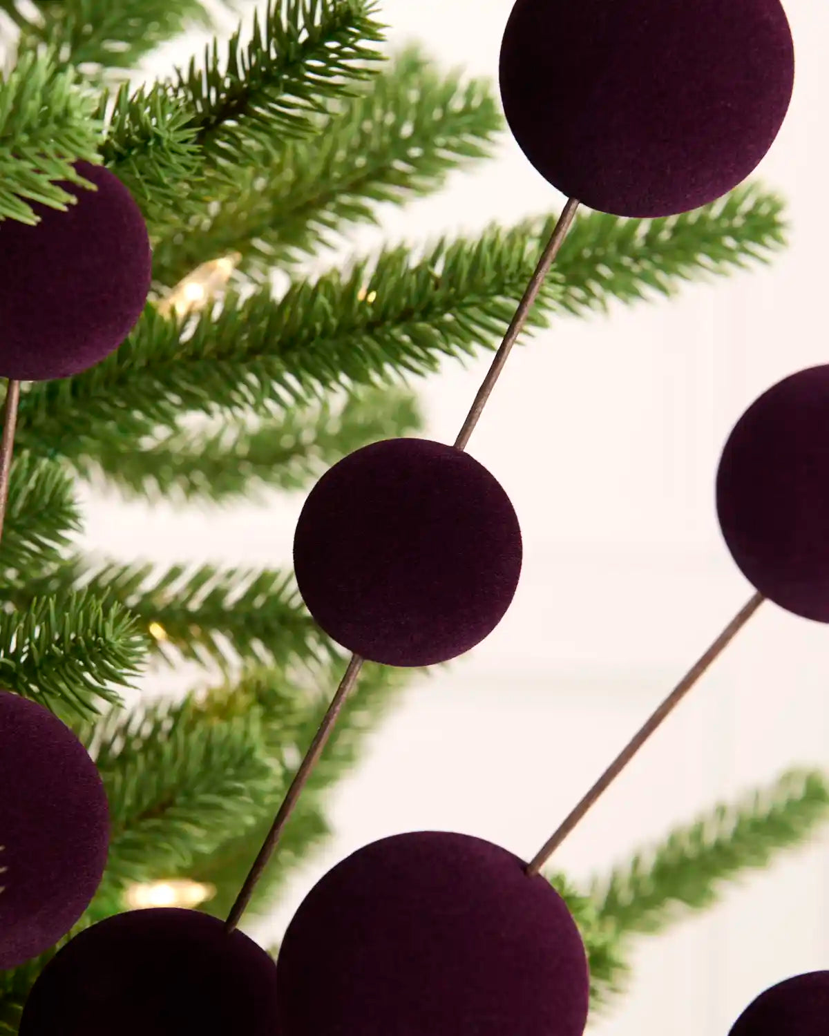 Purple velvet Christmas tree ornaments on thin metal wire stakes, shown hanging against green pine tree branches.