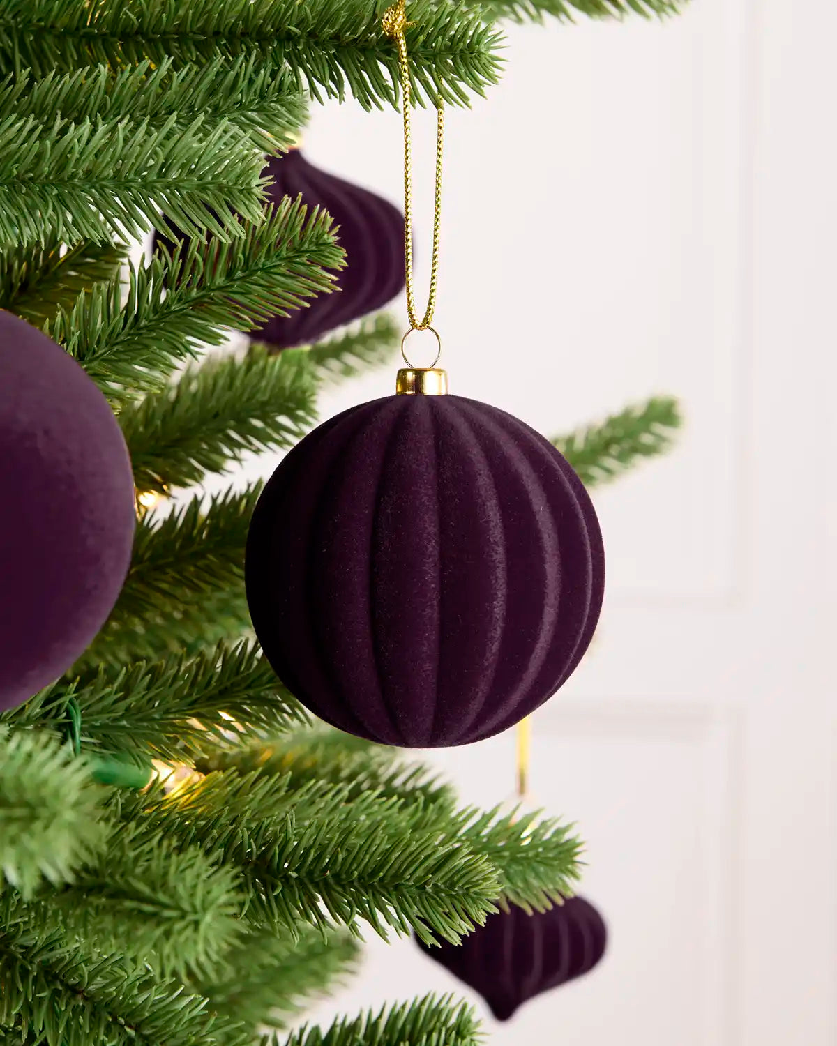 Purple velvet baubles hanging from a Christmas tree, with round and ribbed shape