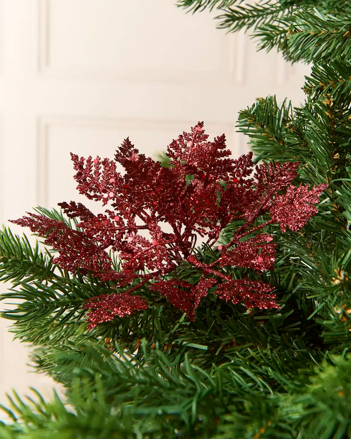 Red Glitter Leaf Pick placed in a Christmas Tree with a cream background