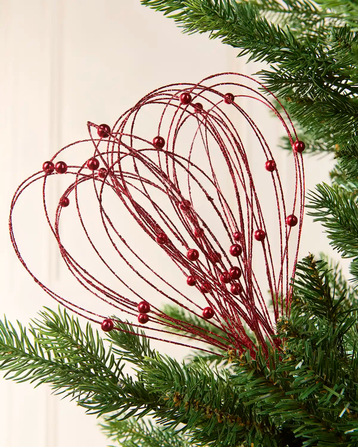 Red Glitter Nest Christmas Tree Pick placed in green Christmas tree branches with a cream background