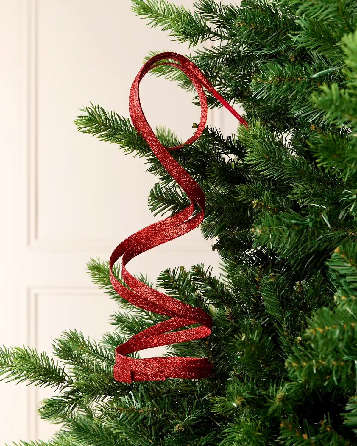 Red Glitter Spiral Swirl Pick hanging from Christmas tree branch with cream background