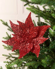 Red Sequin Artificial Poinsettia positioned in Christmas tree branches with a blurry cream background 