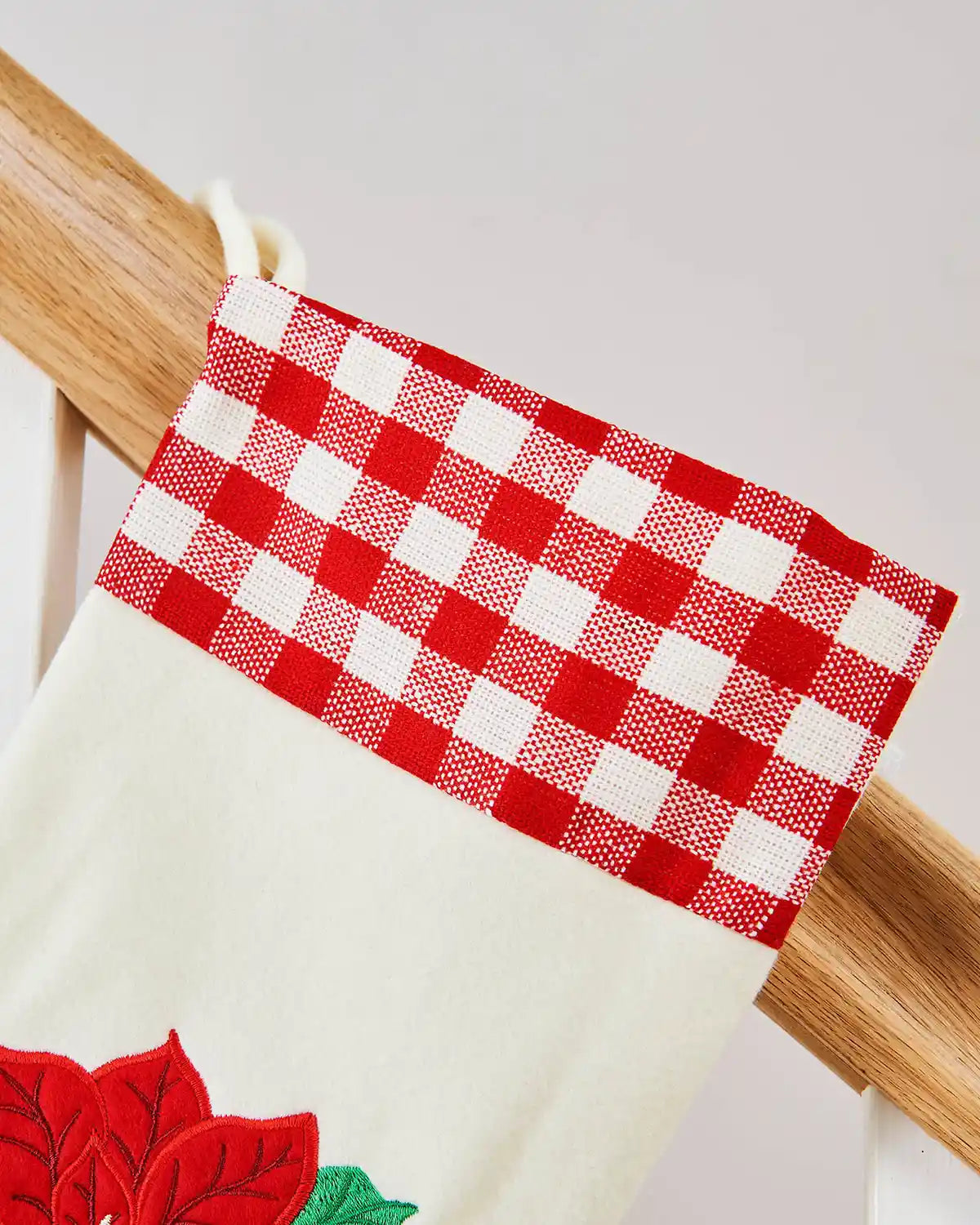 Red and white Tartan design at the top of a White Christmas stocking, hanging on a Wooden Staircase Banister.
