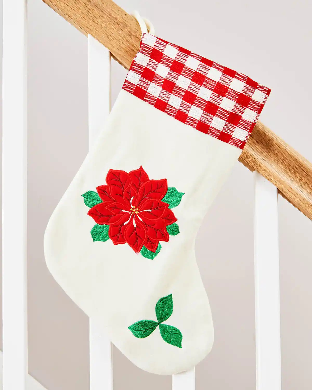 White Christmas stocking with red poinsettia design and red Tartan trim hanging on a wooden Staircase banister.