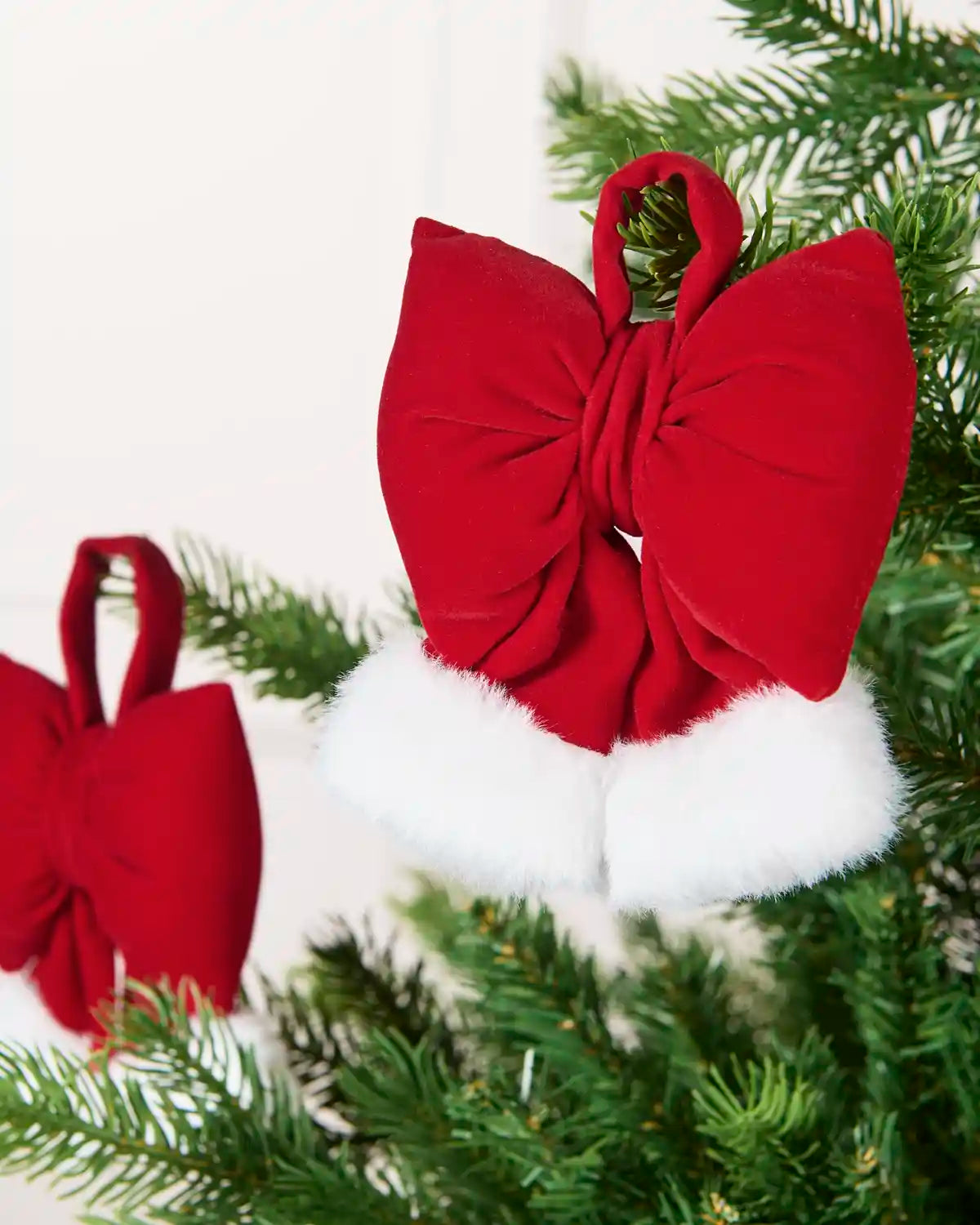 Red and White Mini Velvet Santa Bow hanging from Christmas tree branch with one blurry hanging in the background