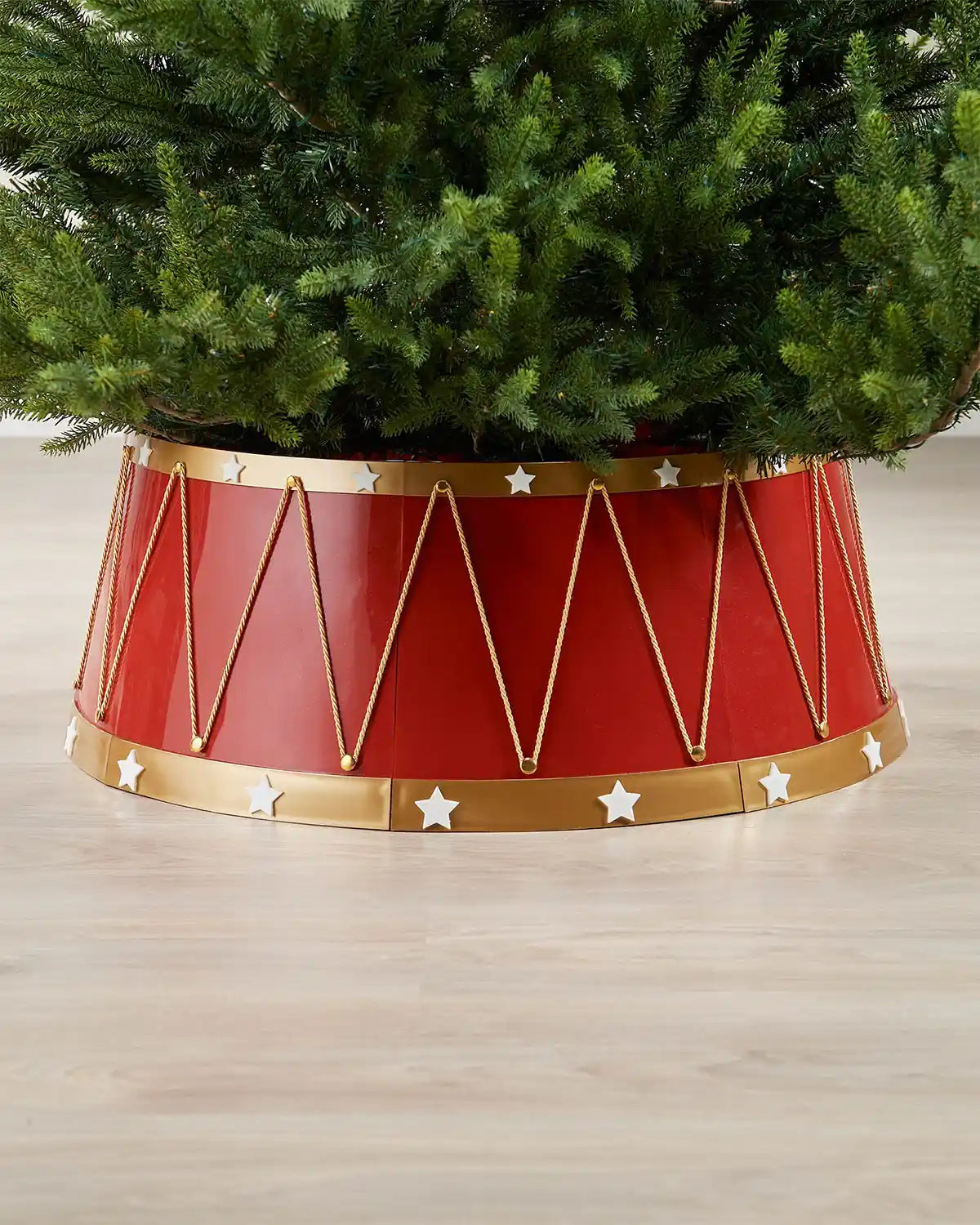 Red and gold tree skirt with star decorations under a Christmas tree on a wooden floor.