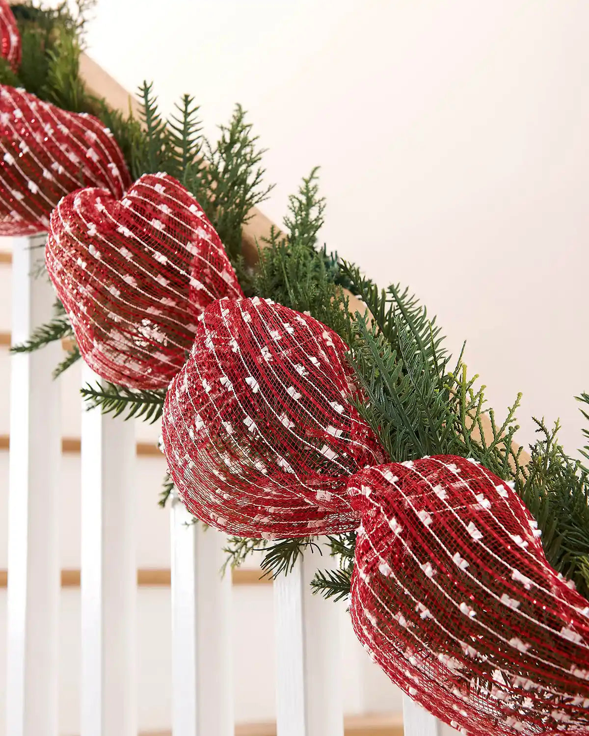 Red and white decorative mesh wrapped around a green garland on a staircase banister 