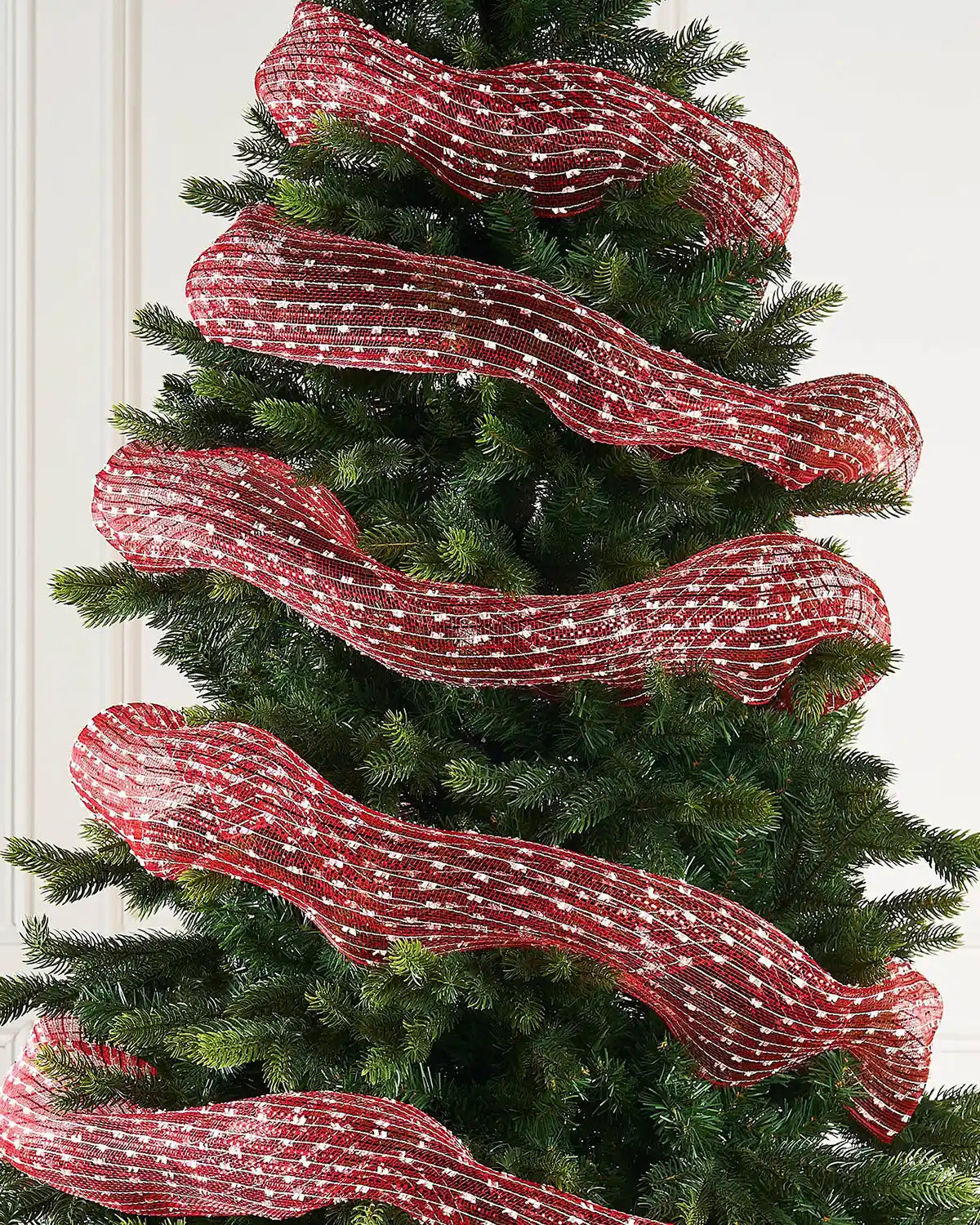 Red and white mesh decorative roll wrapped around a Christmas tree against a cream panel wall