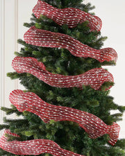 Red and white mesh decorative roll wrapped around a Christmas tree against a cream panel wall