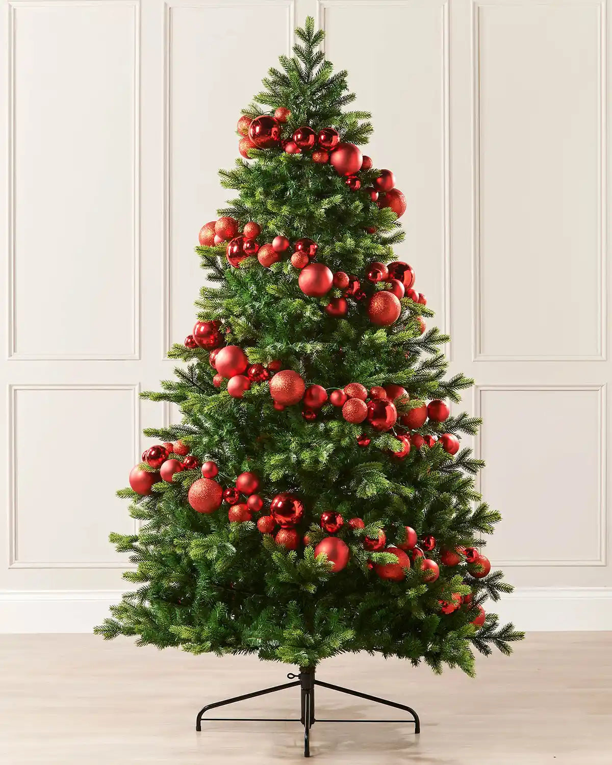 Red bauble garland wrapped around a Christmas tree against a cream panel wall