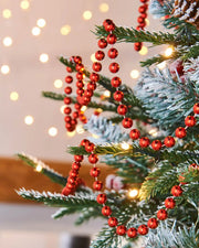 Red bead garland on a Christmas tree with blurred lights in the background