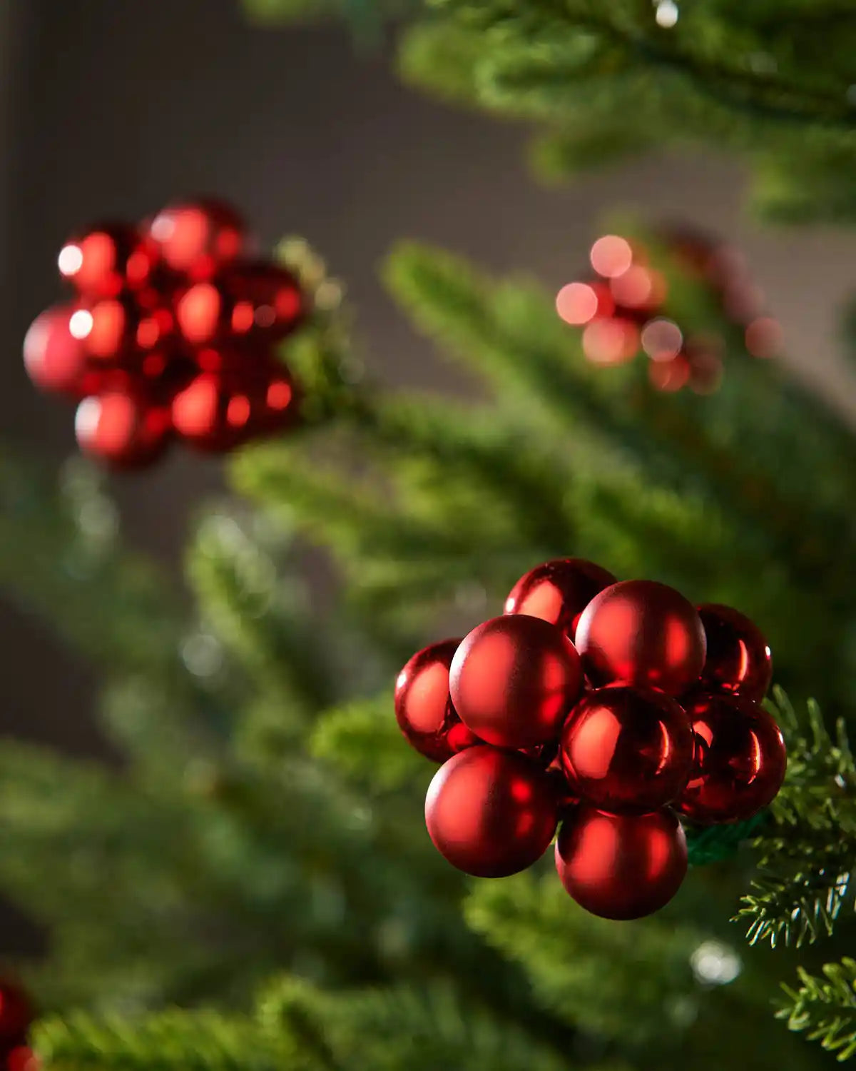 Red berry-like cluster baubles on a Christmas tree against a blurry background