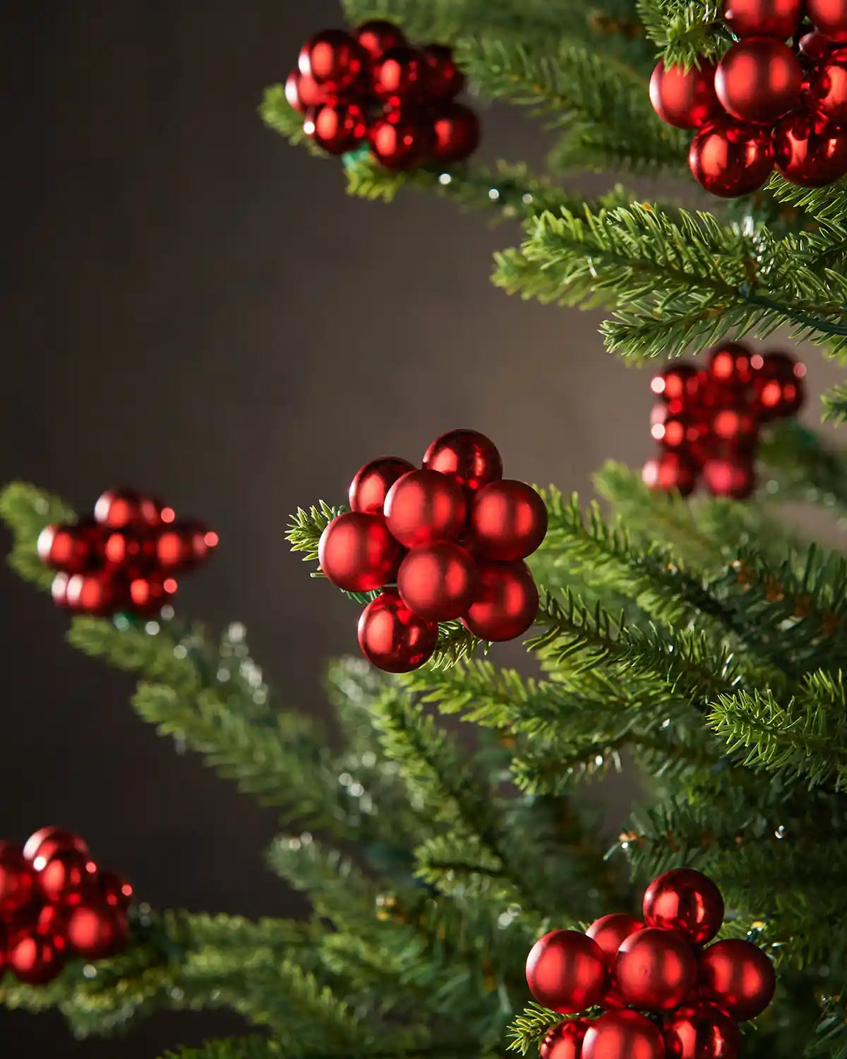 Red berry-like cluster baubles on a Christmas tree against a dark background
