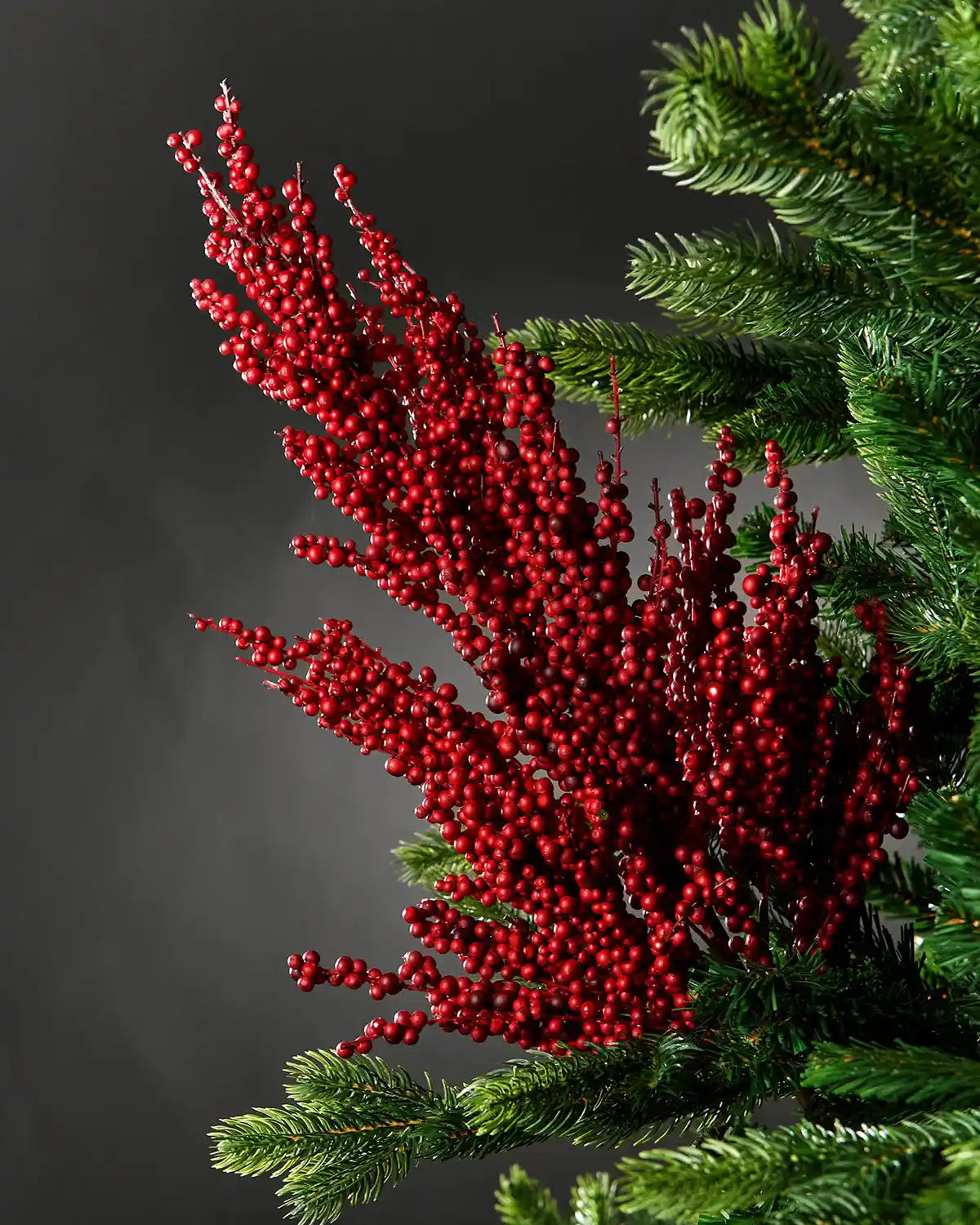 Red berry cluster pick on a Christmas tree against a grey background