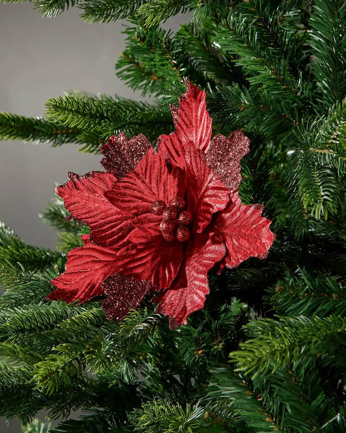 Red decorative Poinsettia on a Green Christmas tree with a Grey wall