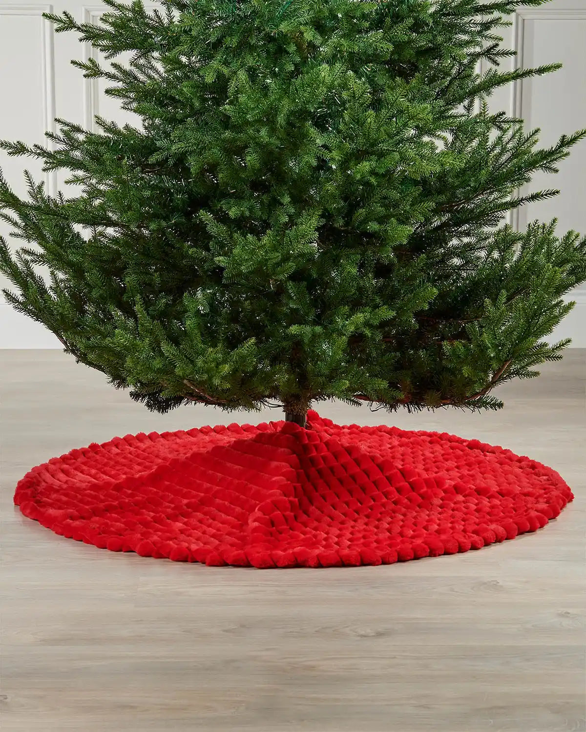 Red faux fur diamond tree skirt on light wooden flooring underneath green Christmas tree