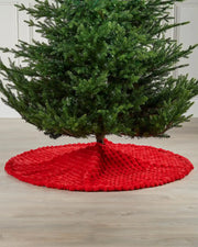 Red faux fur diamond tree skirt on light wooden flooring underneath green Christmas tree