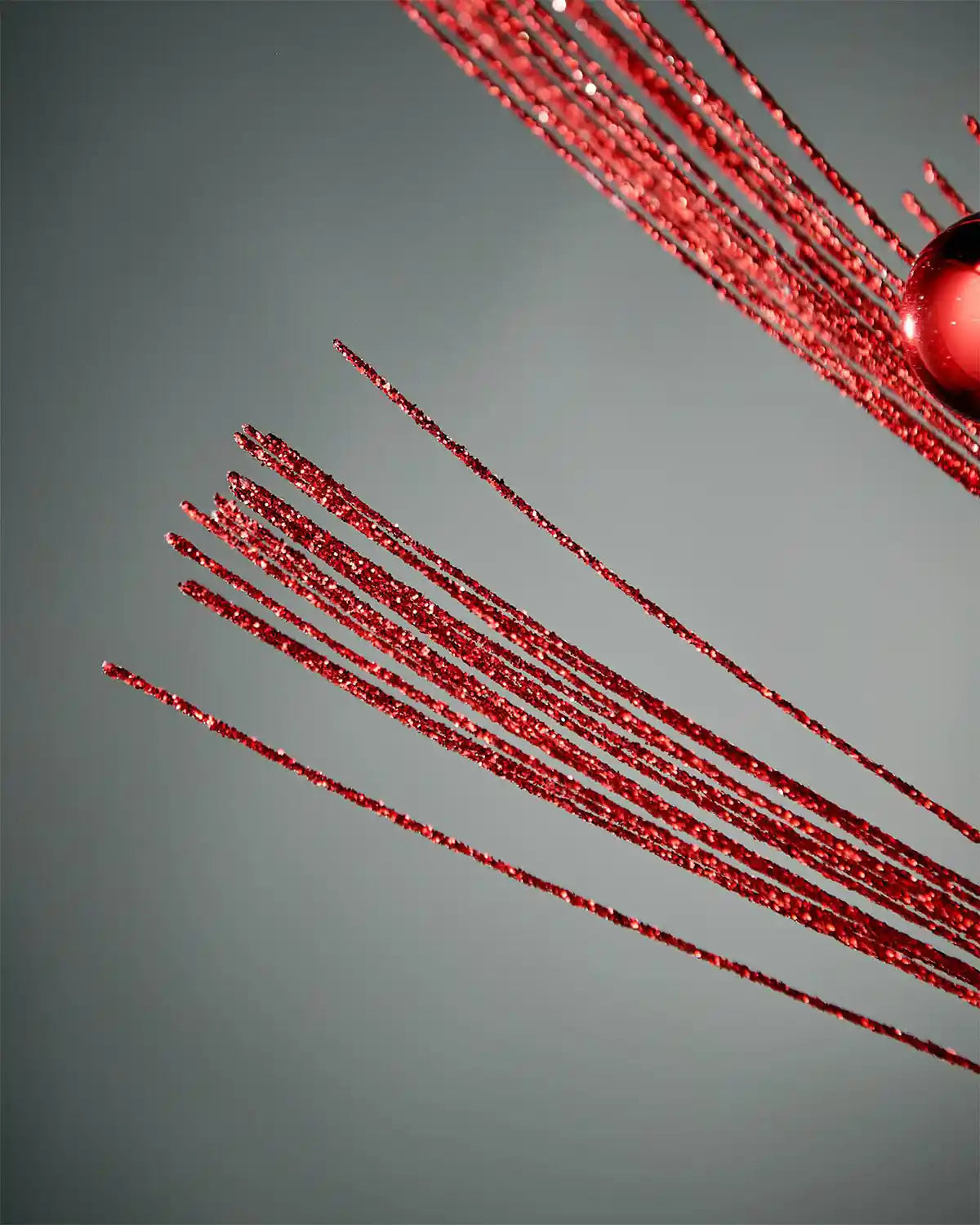 Close-up image of red glitter bauble spray foliage highlighting the sparkle in front of a grey background