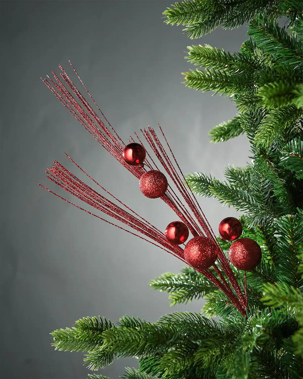 Red glitter bauble spray inside tree in front of grey background