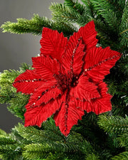 Red glitter-trim artificial poinsettia flower on Christmas tree in front of grey  wall background