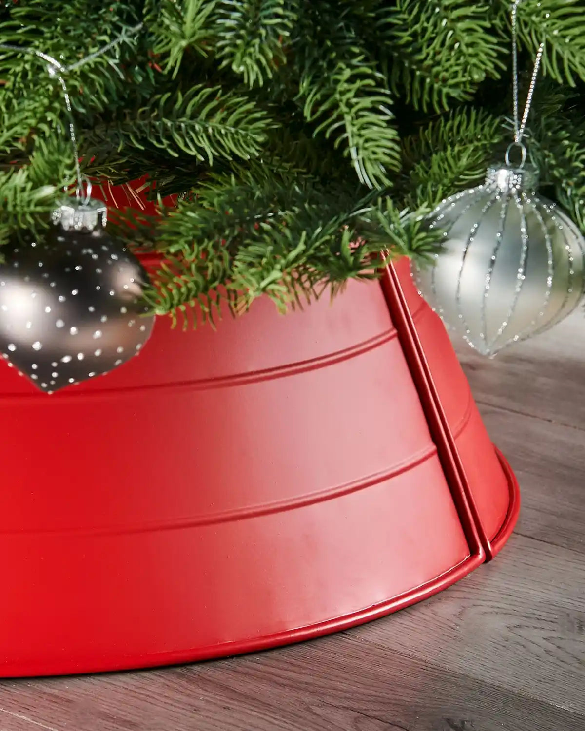 Red metal tree skirt with Christmas tree and ornaments on a wooden floor