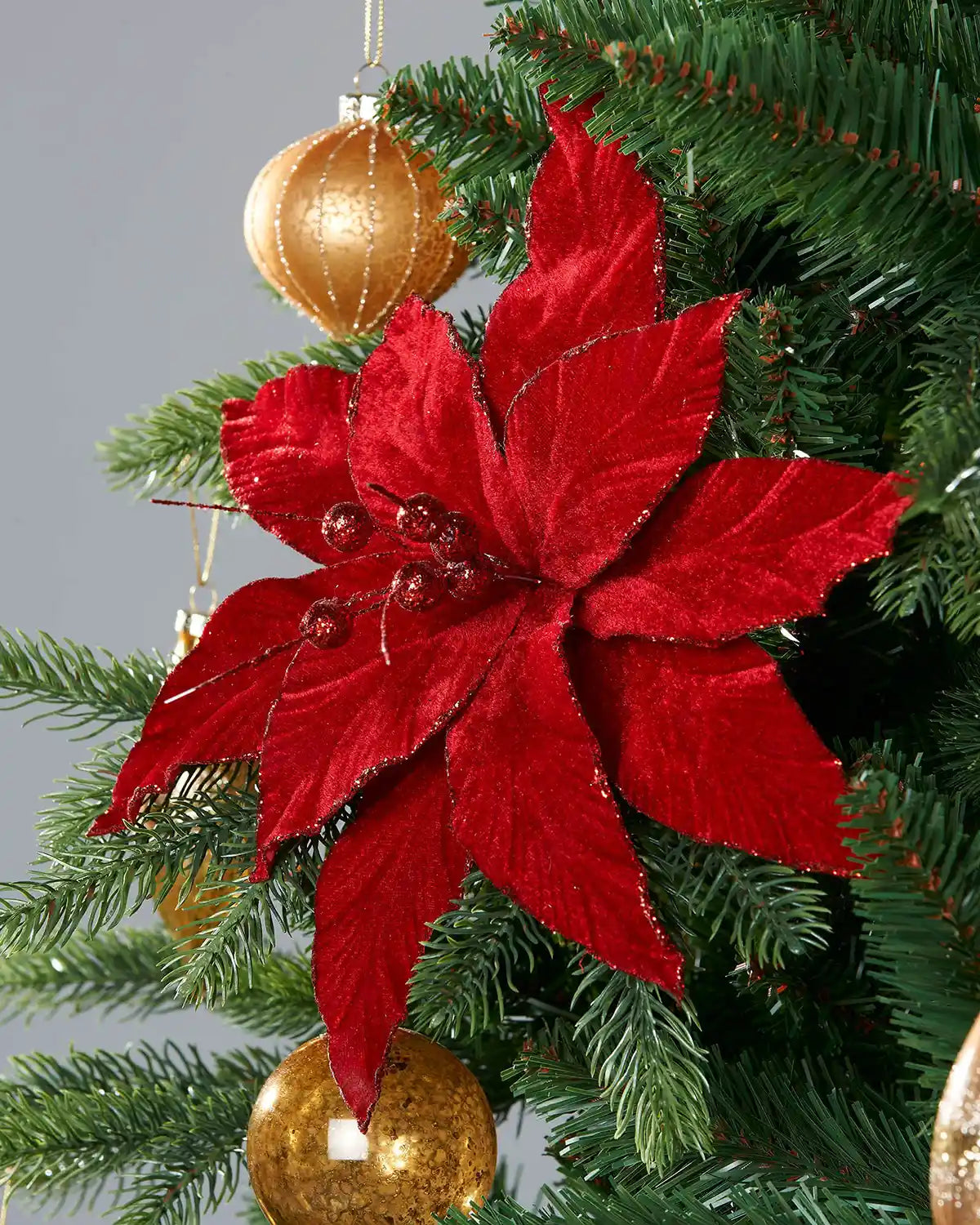 Red poinsettia Christmas pick on a tree with gold baubles.