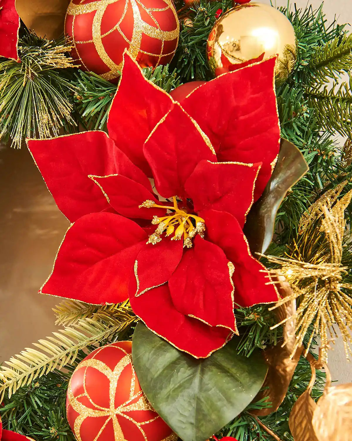 Red poinsettia flower on a Christmas wreath with gold ornaments.