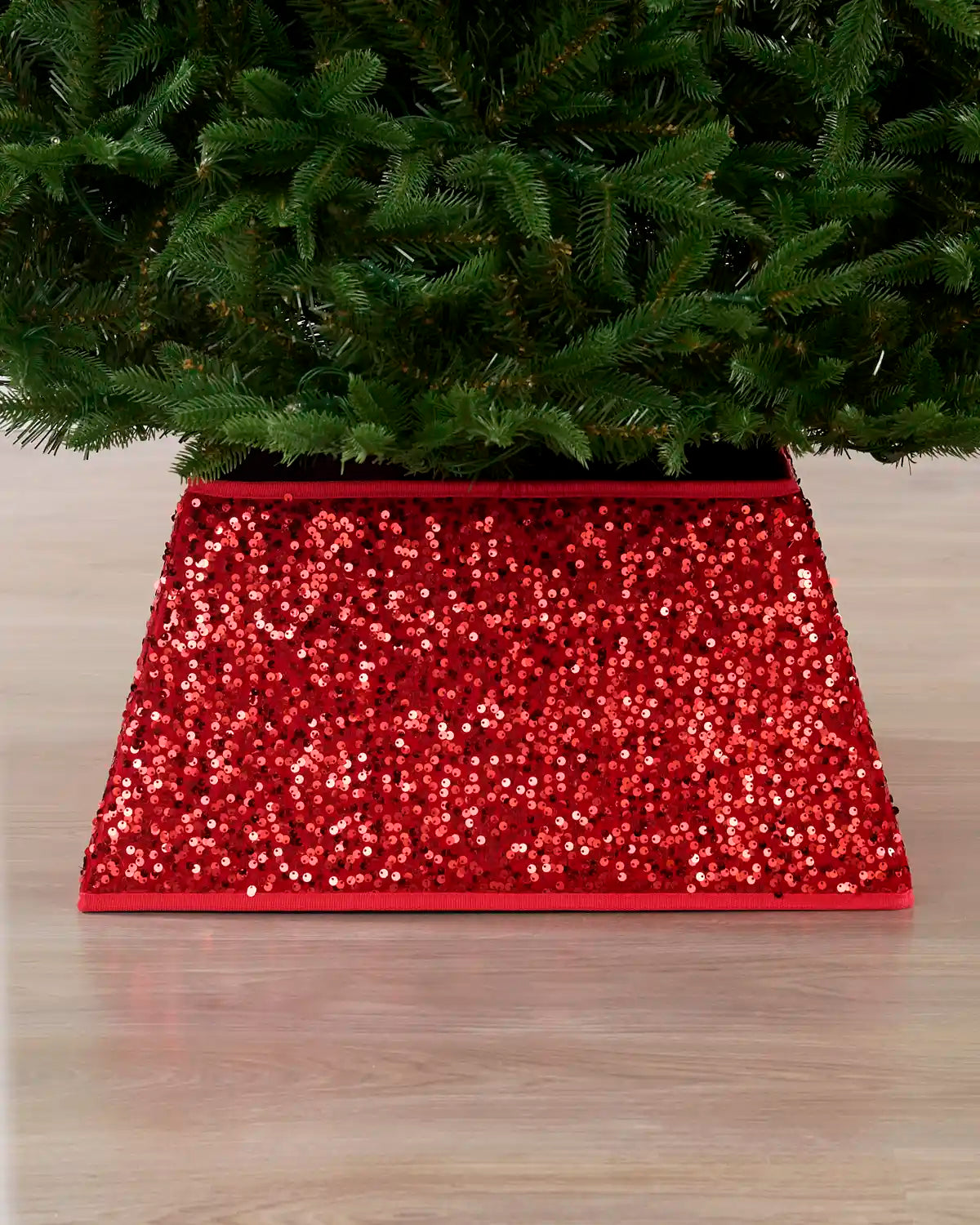 Red sequin square Christmas tree collar under a Christmas tree on a wooden floor