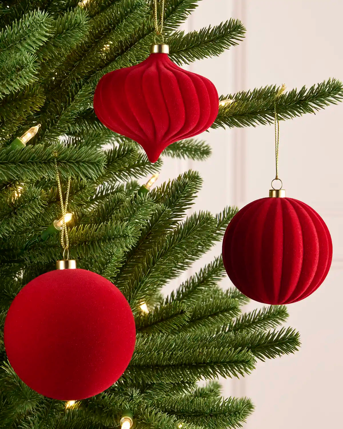 Red spiral, ribbed and smooth velvet baubles hanging on a Christmas tree against a light background