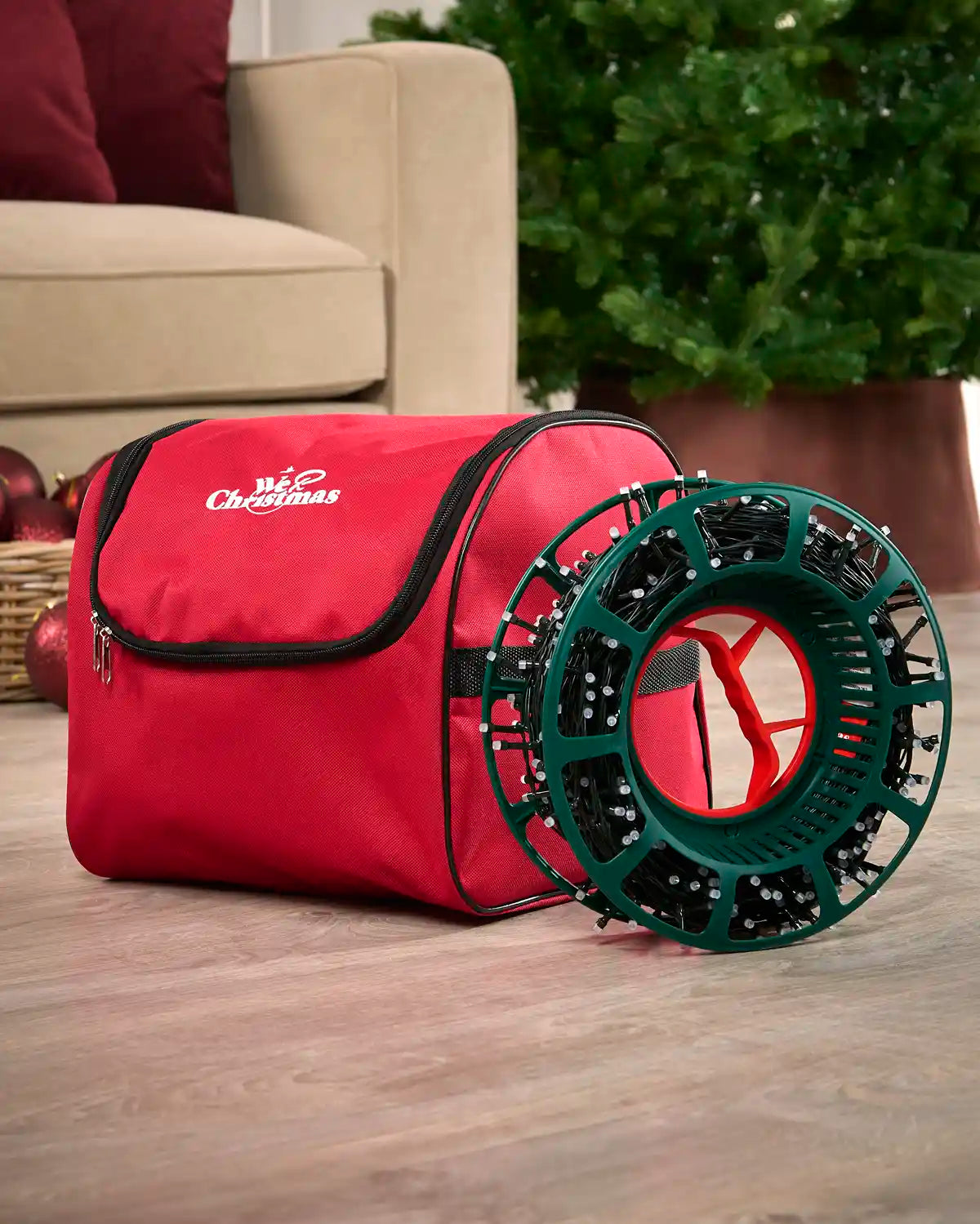Red storage bag with a green reel wrapped with fairy lights on a wooden floor with a Christmas tree and sofa in background