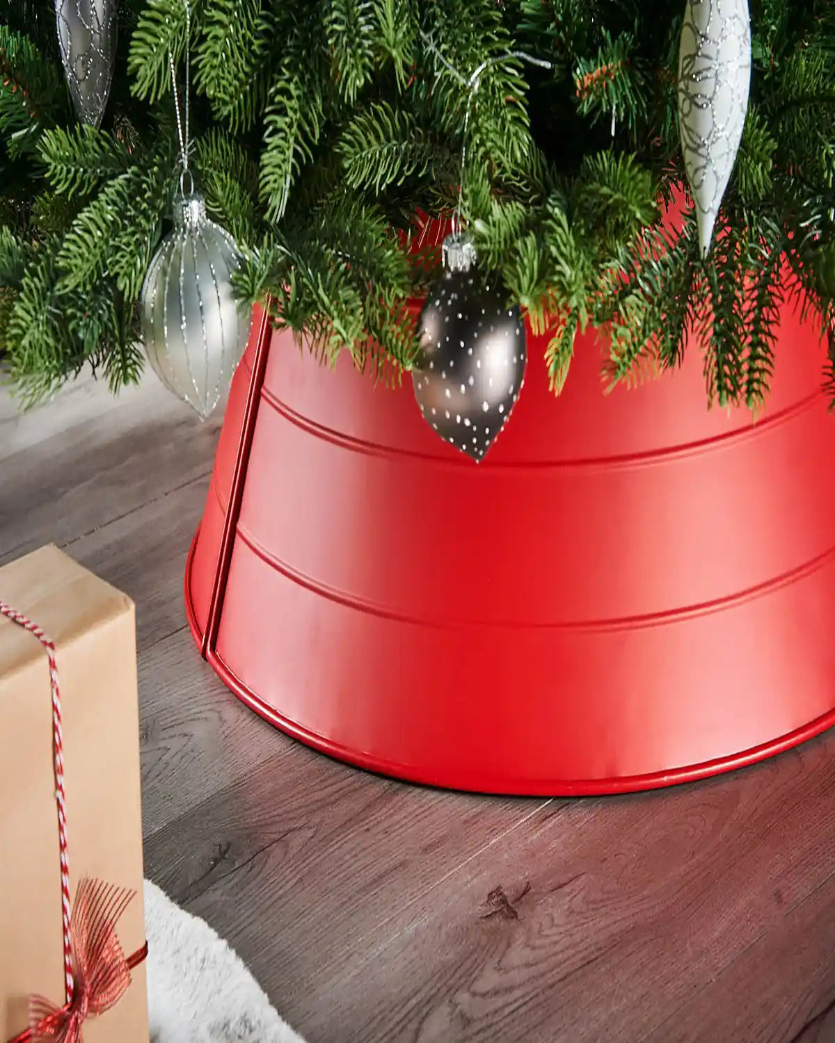 Red tree skirt under a decorated Christmas tree with ornaments and presents on a wooden floor.