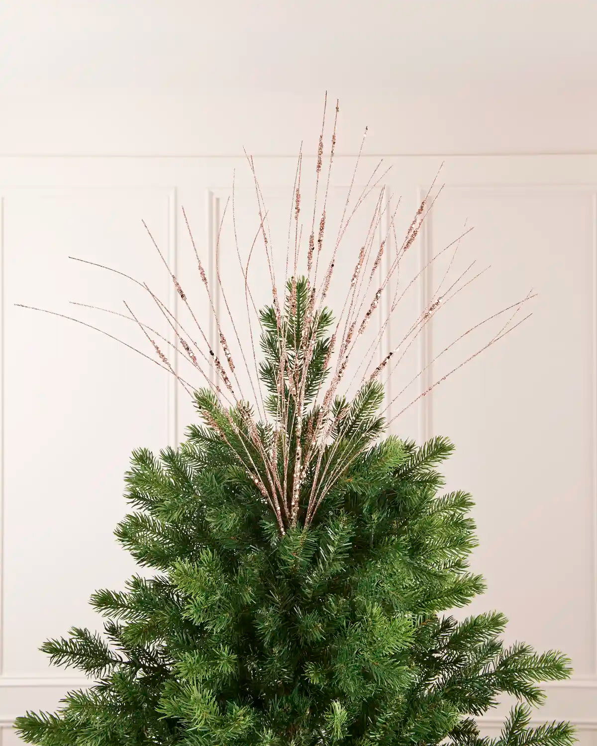 Rose Gold Glitter Wispy Spray displayed at the top of a Christmas tree, with thin glitter-covered stems extending upward and outward
